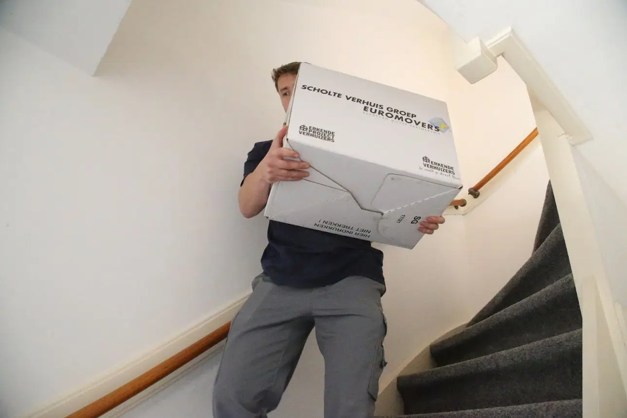SVG-verhuizer draagt een verhuisdoos over de trap in een woning